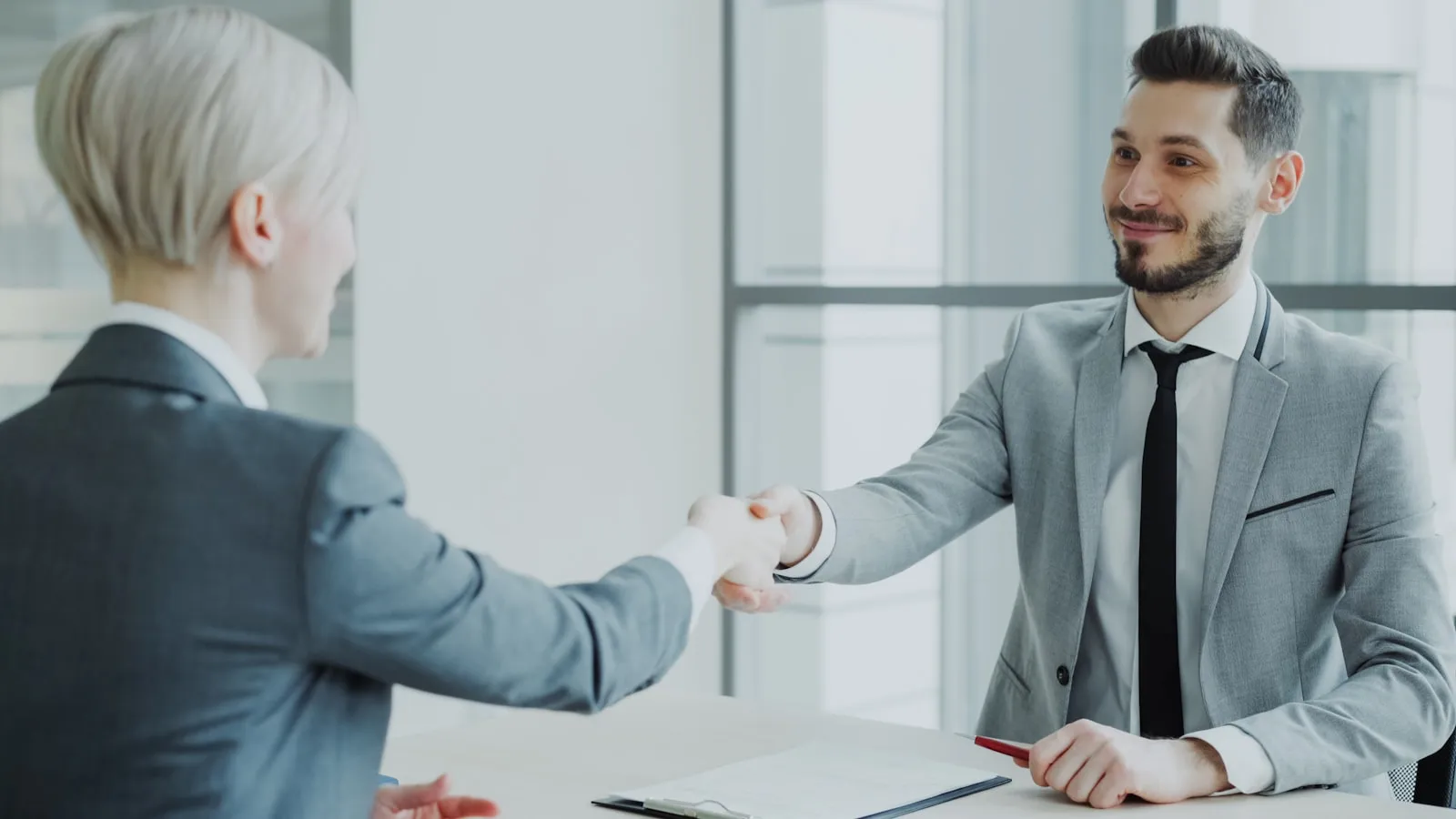 Two professionals shaking hands across a table at a job interview